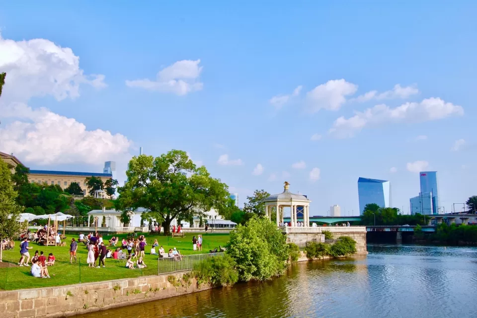 Riverfront park in Philadelphia with white gazebo and skyscrapers in background.